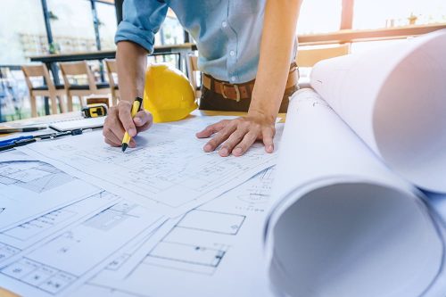 Construction engineer working at blueprint to build large commercial buildings in office. Engineering tools and construction concept.